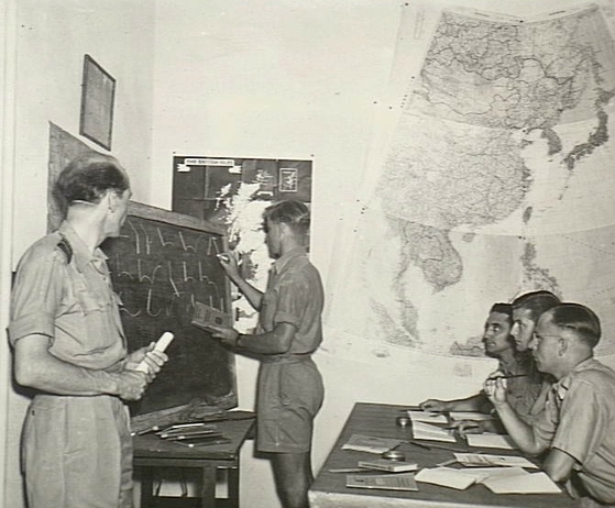A man writing shorthand on a blackboard in a classroom while four other men look on