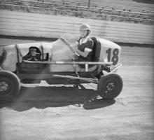 Young woman smiling while driving a 1930s racing car along a speedway